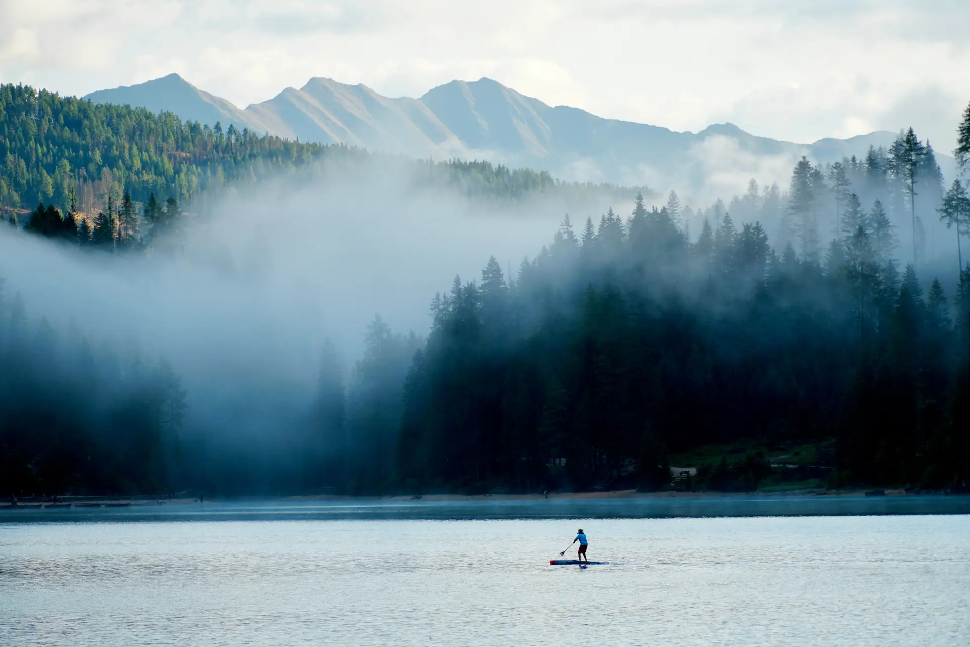 Solitary paddleboarder on glassy alpine water