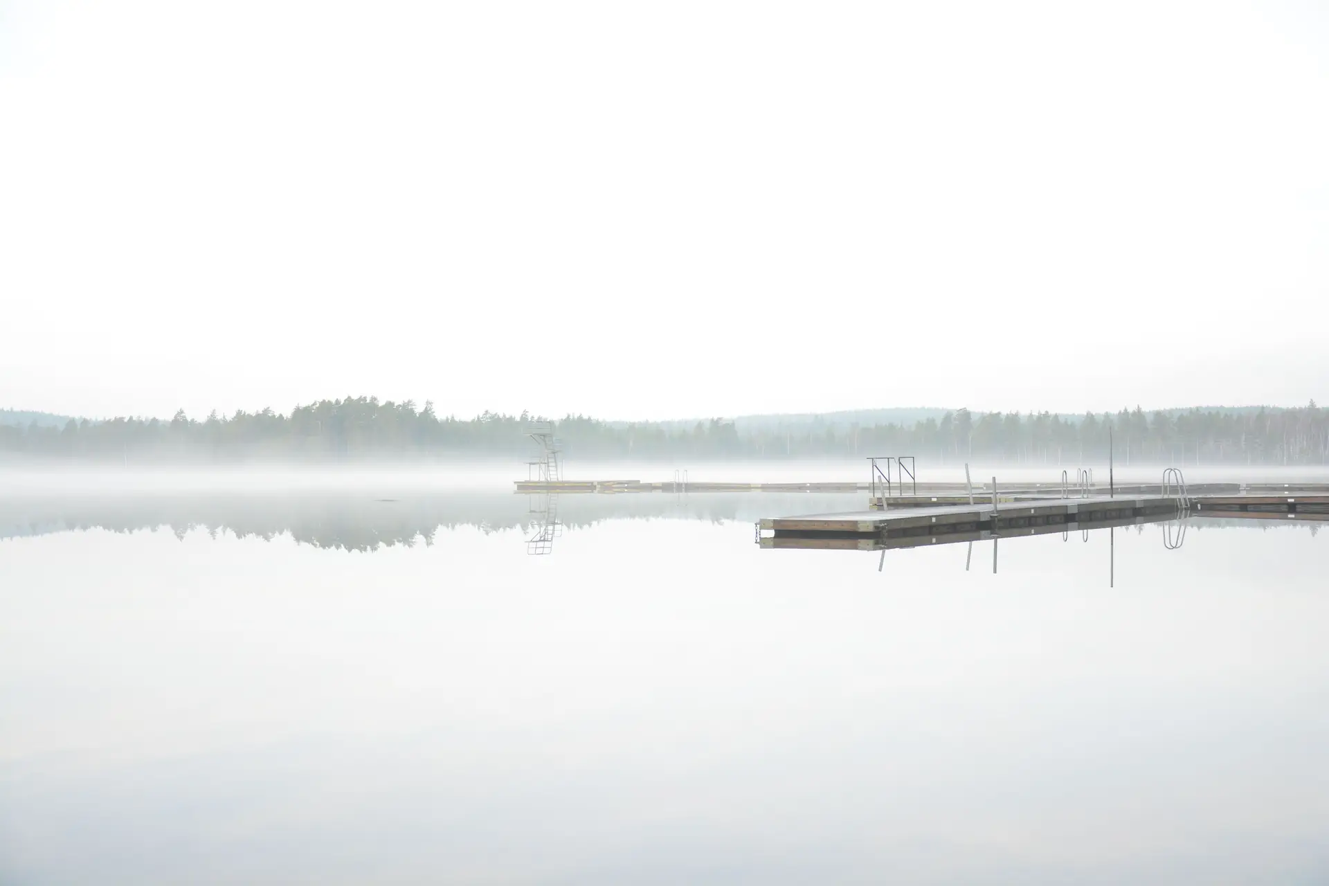 Misty Canadian dawn lake with a wooden pier and still pine reflection