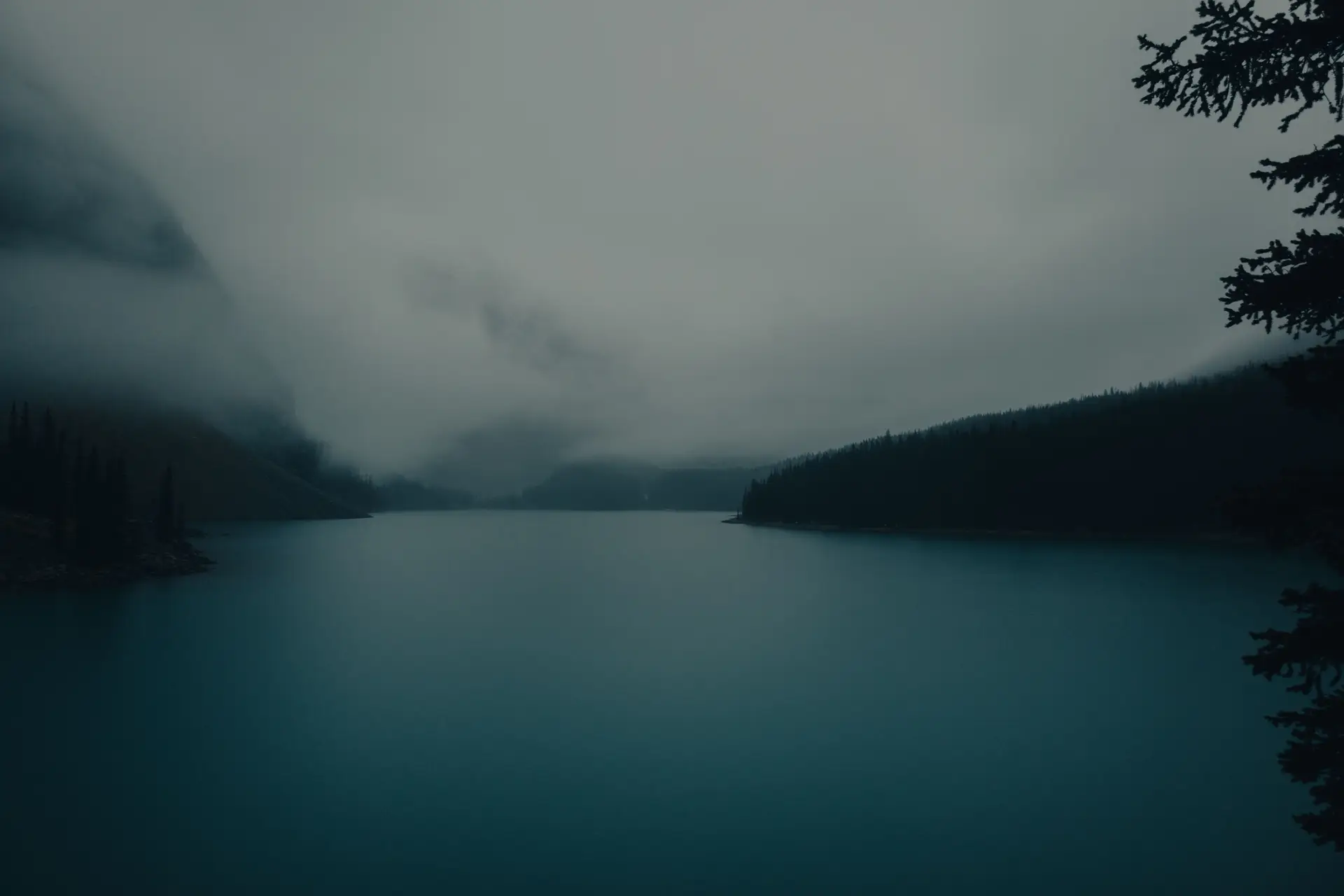 Foggy view of Moraine Lake surrounded by dense forest in Banff National Park